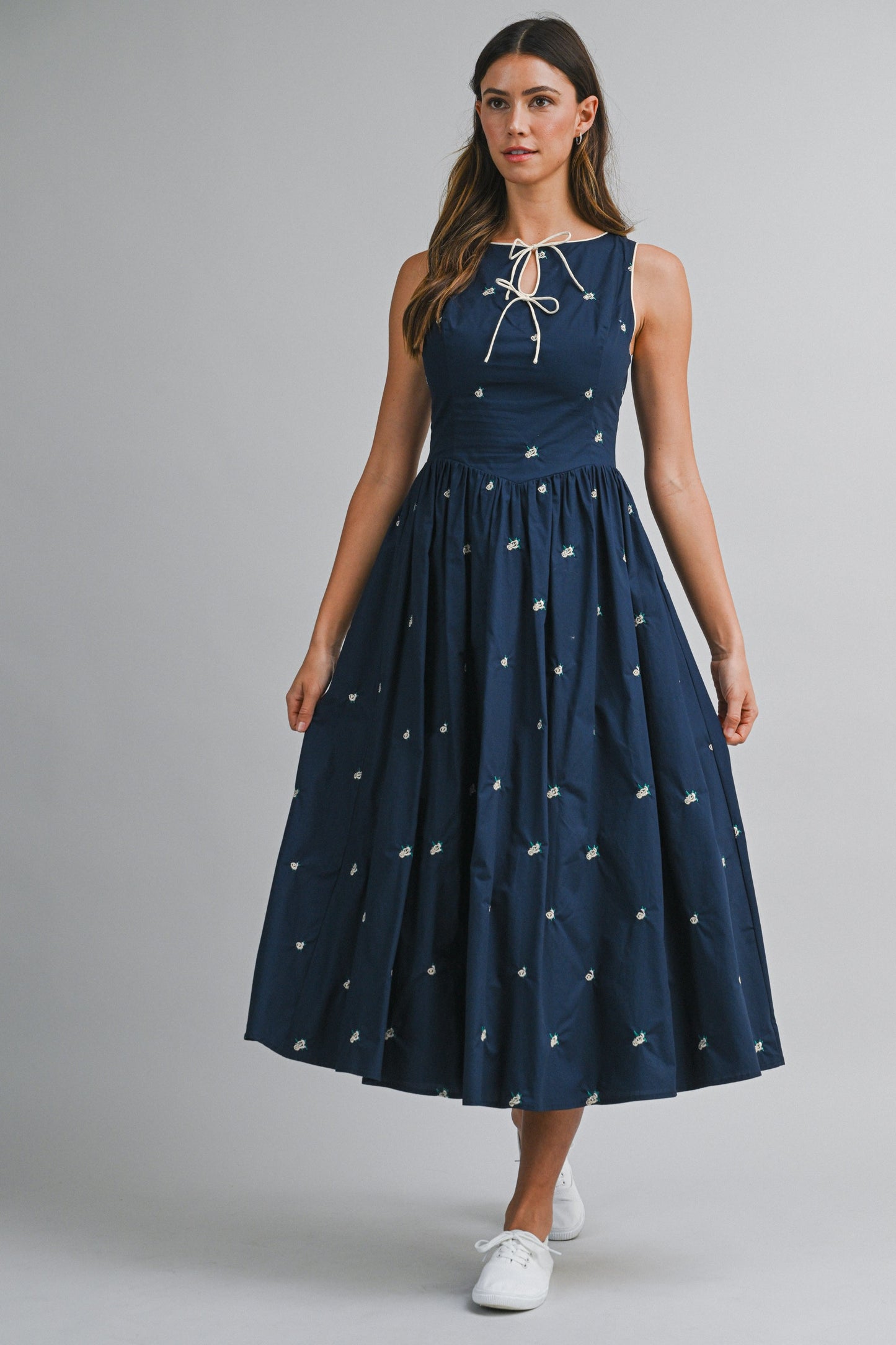 A navy sleeveless midi dress with floral embroidery, a keyhole self-tie neckline, fitted bodice, smocked back, and softly gathered A-line skirt.