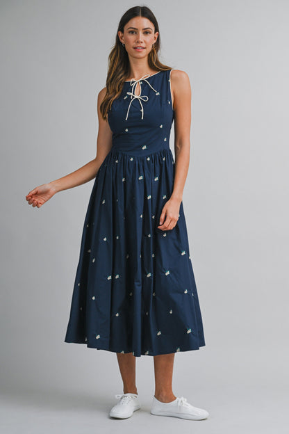 A navy sleeveless midi dress with floral embroidery, a keyhole self-tie neckline, fitted bodice, smocked back, and softly gathered A-line skirt.