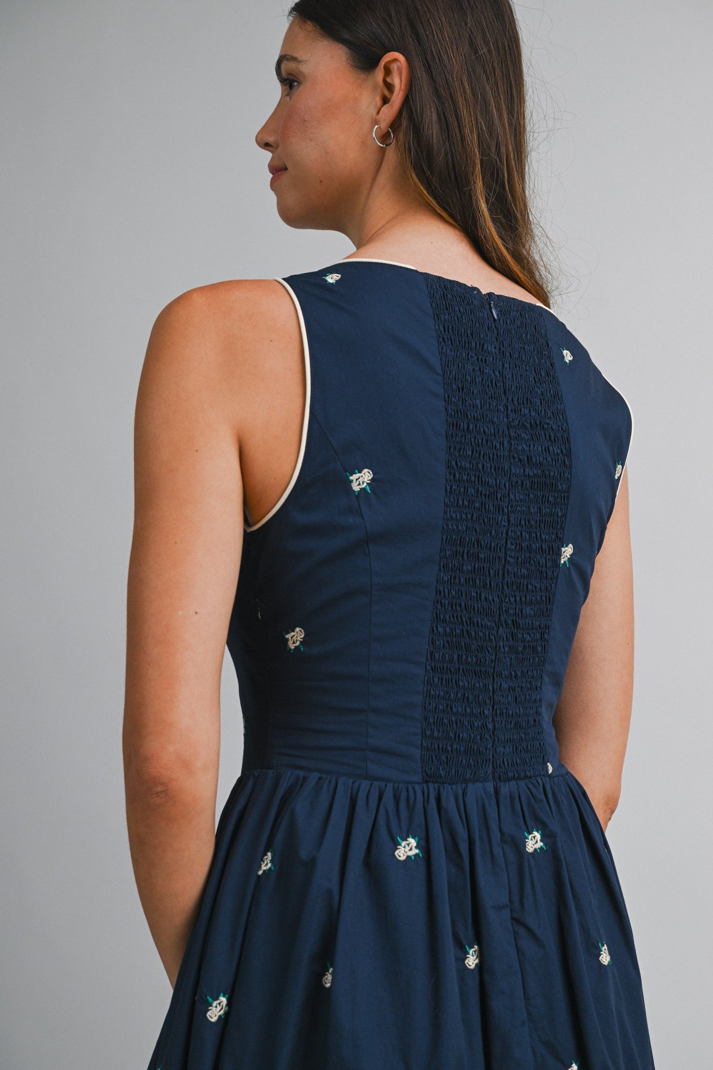 A navy sleeveless midi dress with floral embroidery, a keyhole self-tie neckline, fitted bodice, smocked back, and softly gathered A-line skirt.