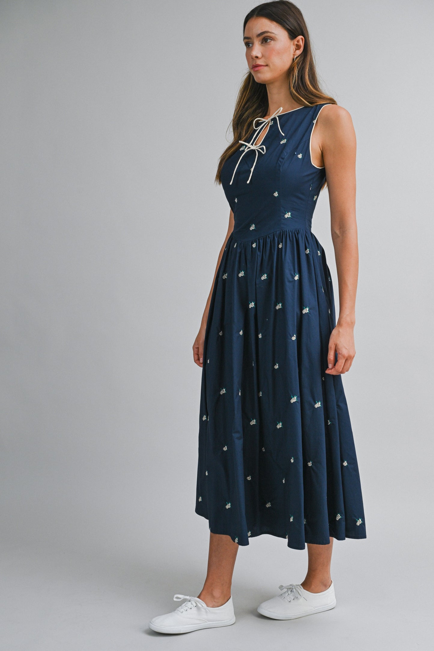 A navy sleeveless midi dress with floral embroidery, a keyhole self-tie neckline, fitted bodice, smocked back, and softly gathered A-line skirt.