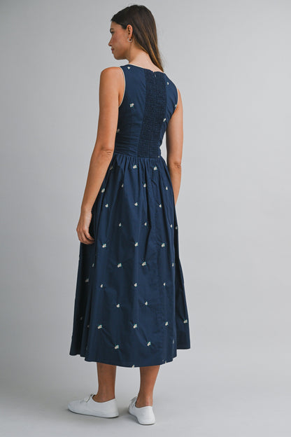 A navy sleeveless midi dress with floral embroidery, a keyhole self-tie neckline, fitted bodice, smocked back, and softly gathered A-line skirt.