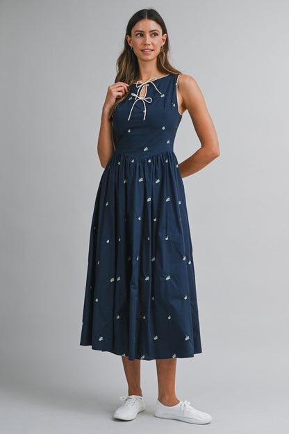 A navy sleeveless midi dress with floral embroidery, a keyhole self-tie neckline, fitted bodice, smocked back, and softly gathered A-line skirt.