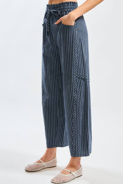 A pair of women's high-waisted wide-leg cropped pants featuring a indigo and white vertical pinstripe pattern with a gathered elastic drawstring waistband and front pockets.