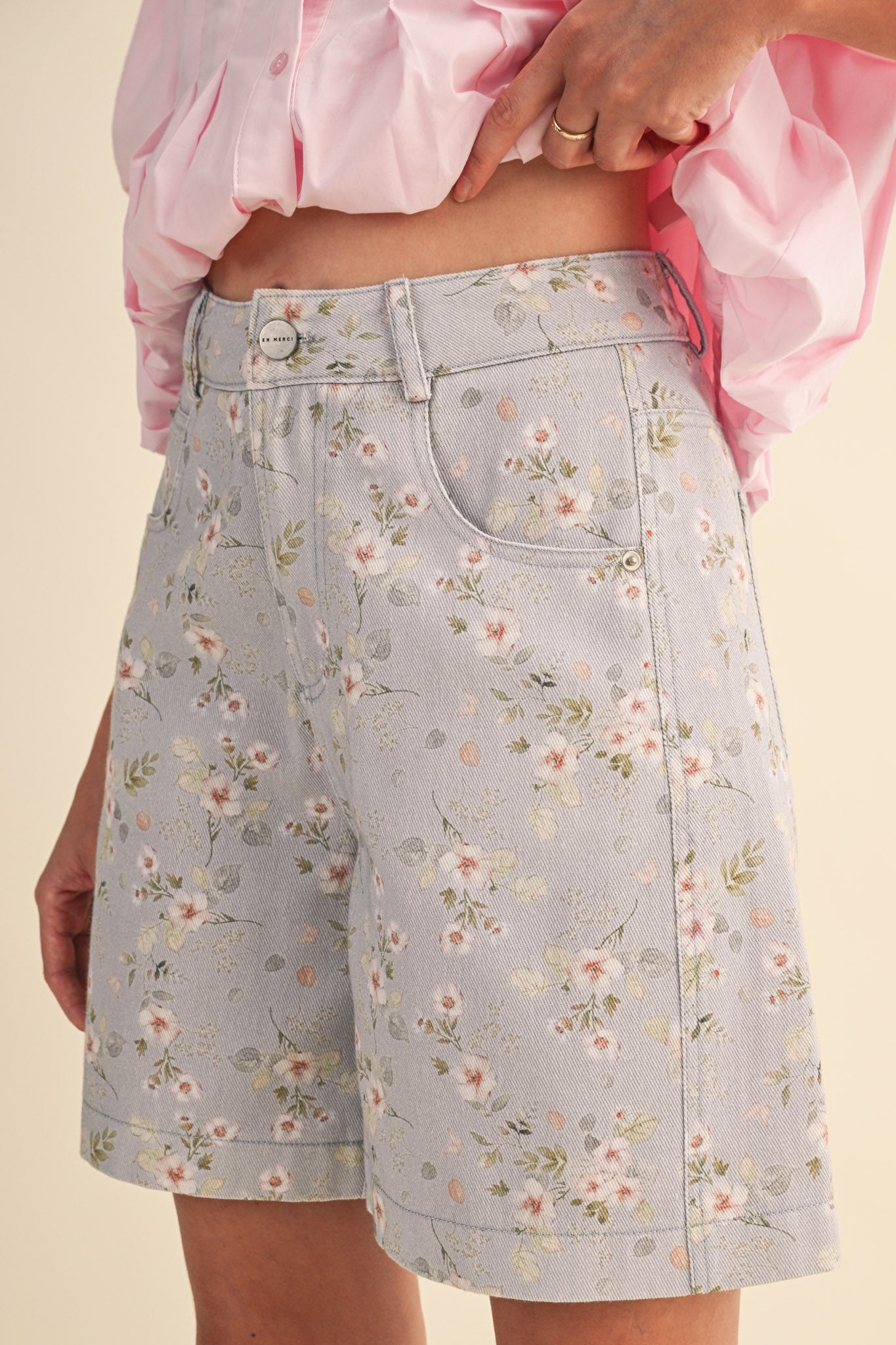A pair of high-waisted women's light denim shorts in a light wash with a delicate pink and green floral print, featuring a modest mid-length hem and classic front pockets.