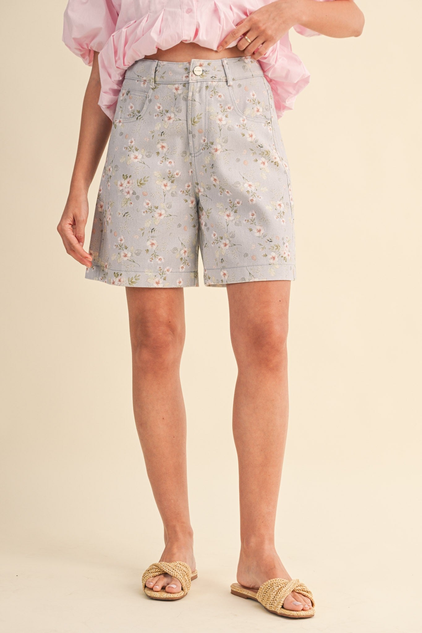 A pair of high-waisted women's light denim shorts in a light wash with a delicate pink and green floral print, featuring a modest mid-length hem and classic front pockets.