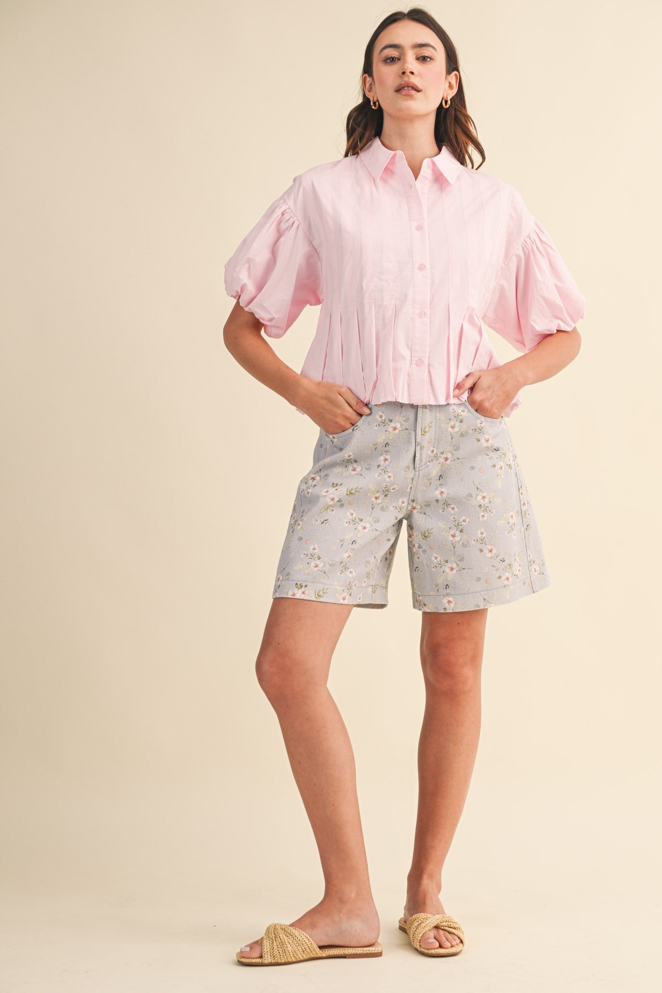 A pair of high-waisted women's light denim shorts in a light wash with a delicate pink and green floral print, featuring a modest mid-length hem and classic front pockets.