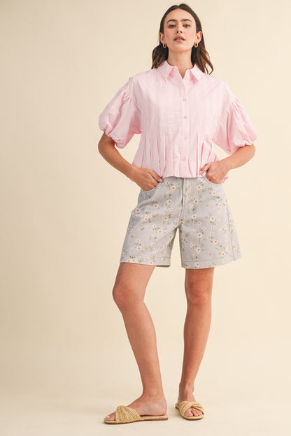 A pair of high-waisted women's light denim shorts in a light wash with a delicate pink and green floral print, featuring a modest mid-length hem and classic front pockets.