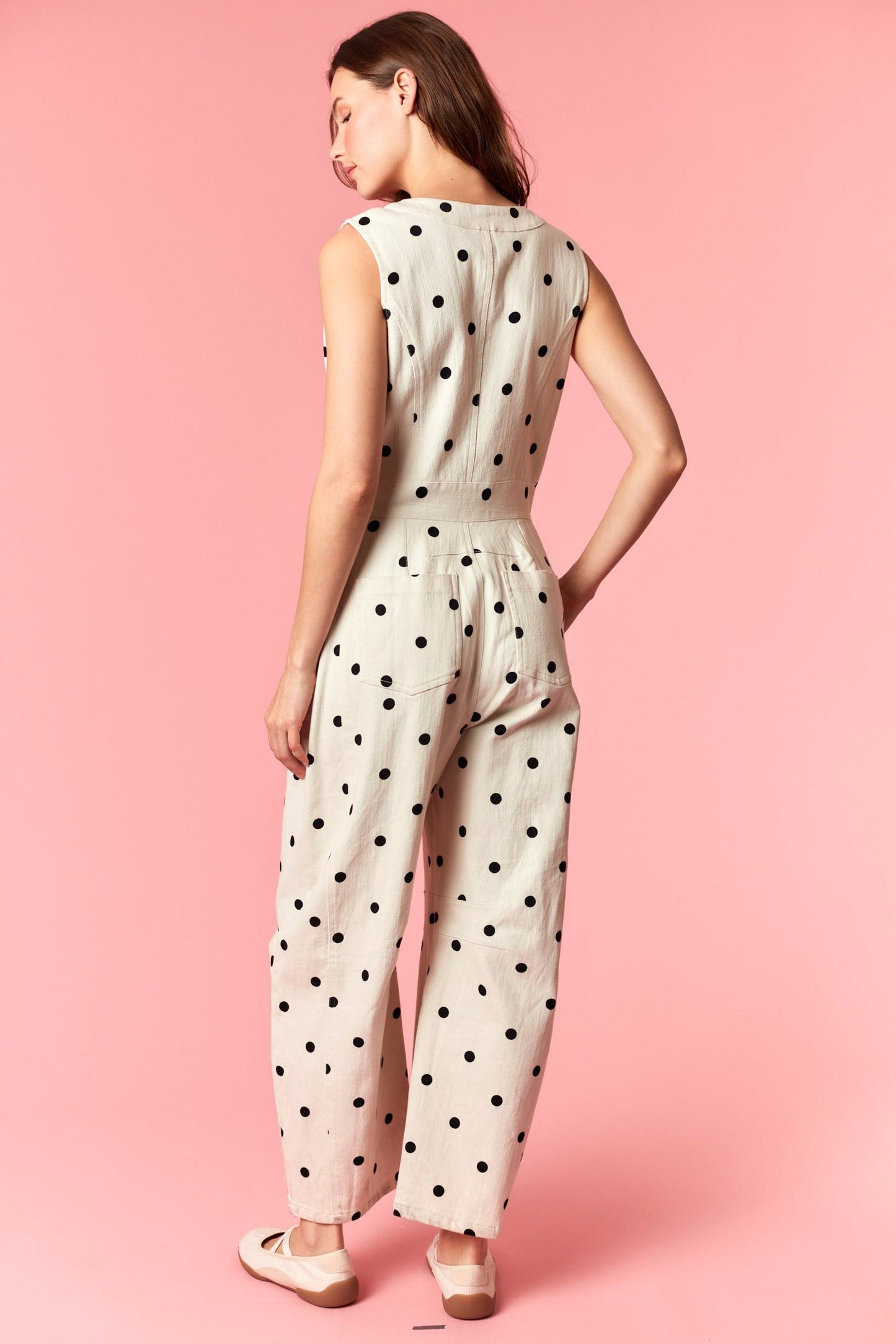 A sleeveless wide-leg jumpsuit in ivory and black polka dot featuring a functional front zipper closure, a round neckline, structured front pleating, and side pockets.