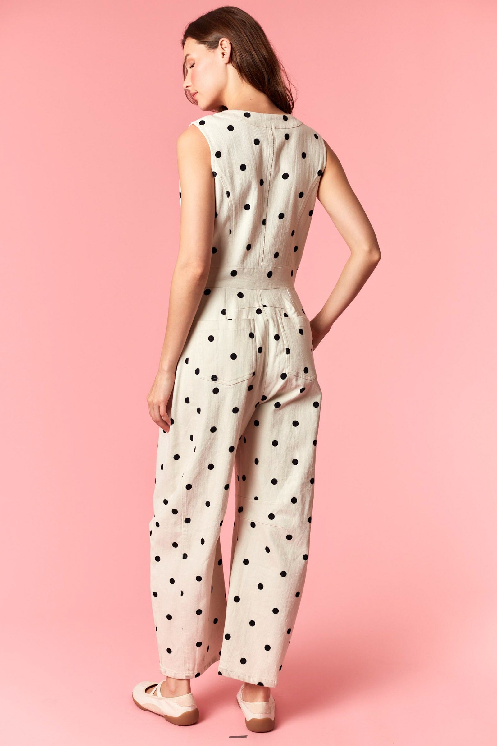 A sleeveless wide-leg jumpsuit in ivory and black polka dot featuring a functional front zipper closure, a round neckline, structured front pleating, and side pockets.