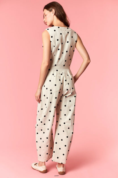 A sleeveless wide-leg jumpsuit in ivory and black polka dot featuring a functional front zipper closure, a round neckline, structured front pleating, and side pockets.