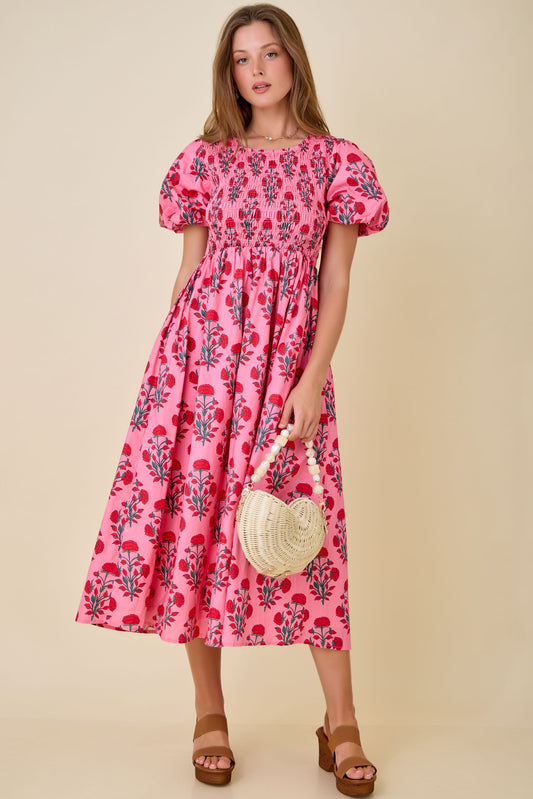 A short-sleeve fuchsia and red floral midi dress featuring a fully smocked bodice, a square neckline, and voluminous puff sleeves with elastic cuffs.