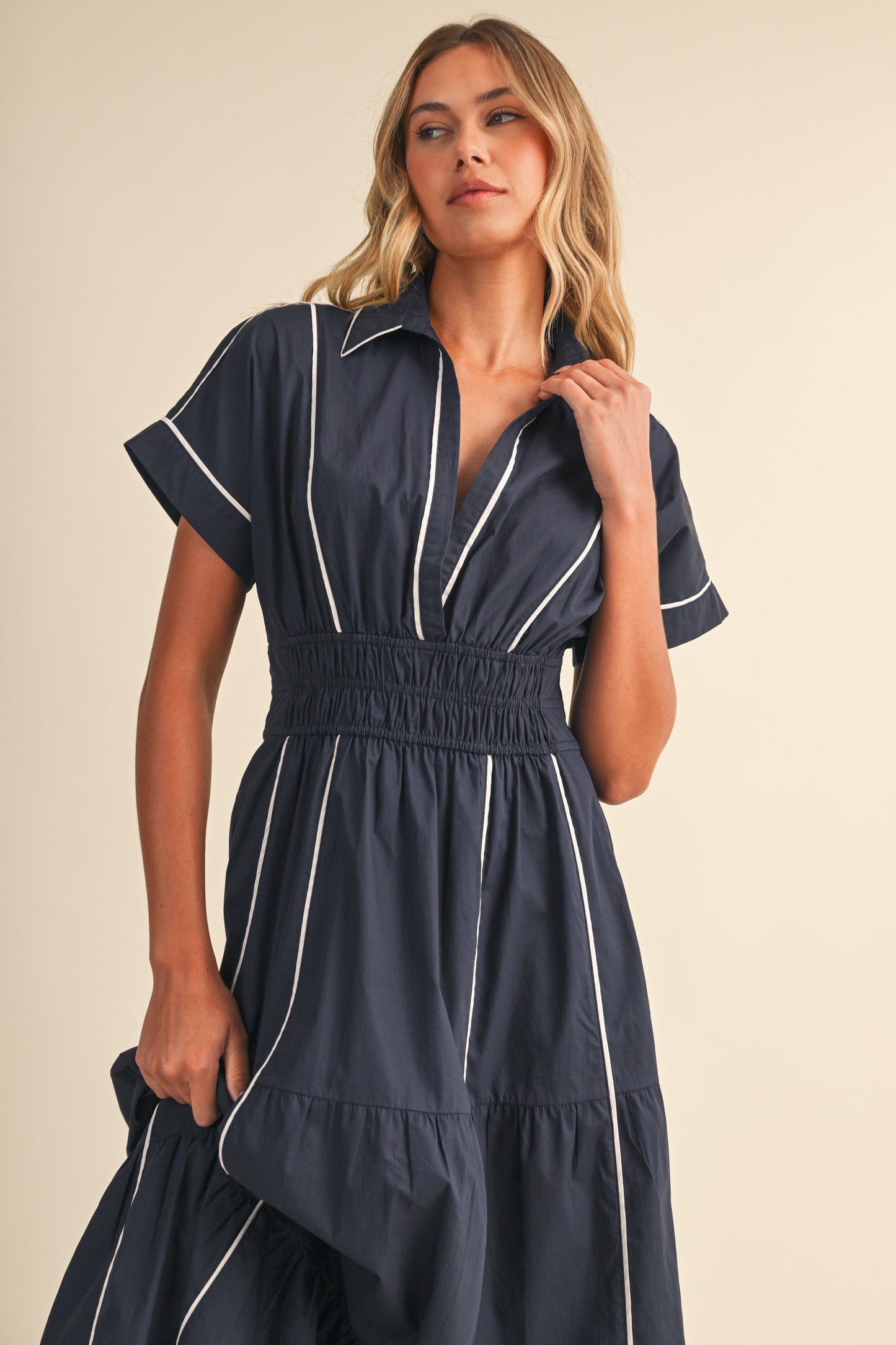 A short-sleeve navy blue shirt maxi dress featuring a classic collar, white vertical contrast piping, a thick smocked elastic waistband, and a tiered A-line skirt.