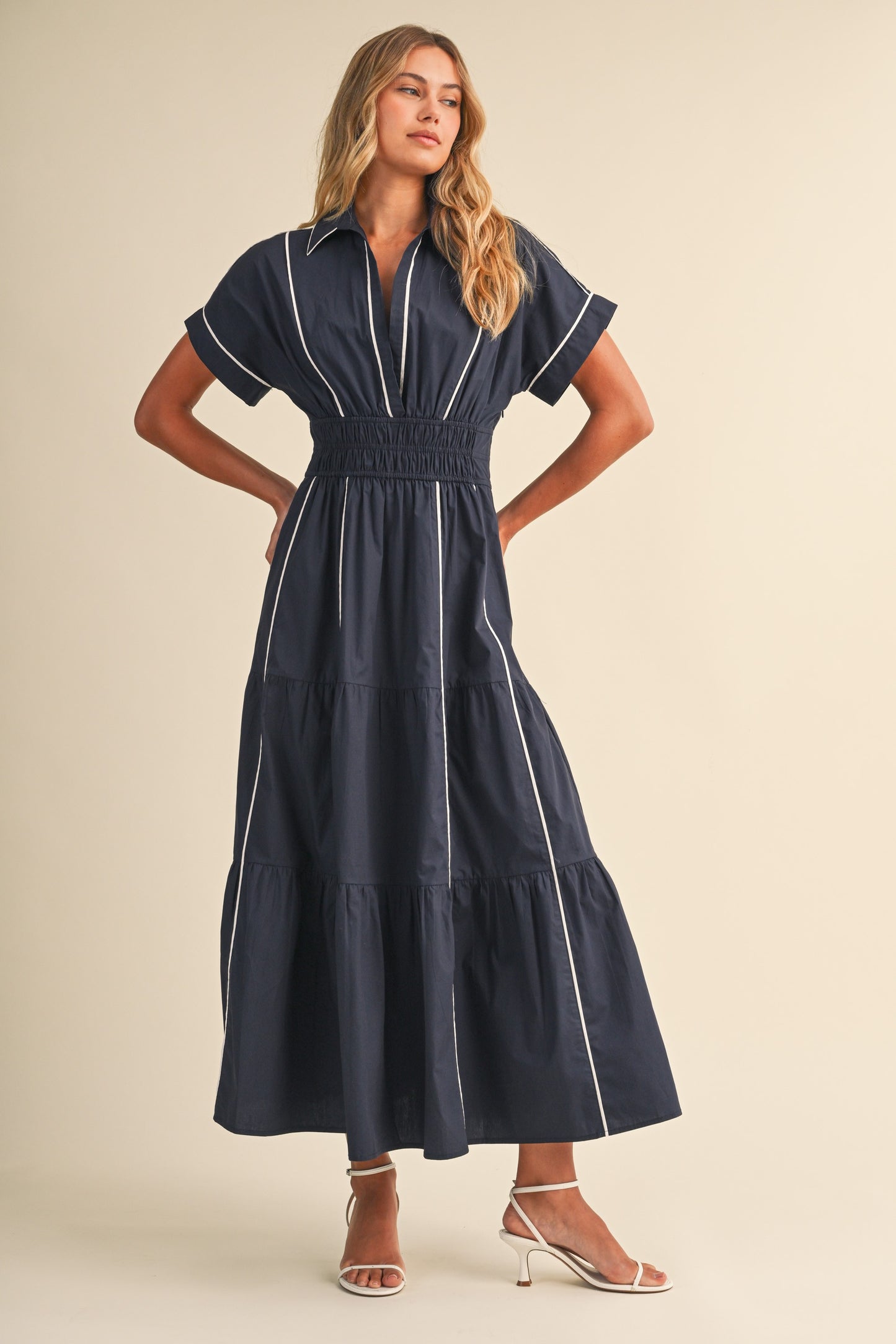 A short-sleeve navy blue shirt maxi dress featuring a classic collar, white vertical contrast piping, a thick smocked elastic waistband, and a tiered A-line skirt.