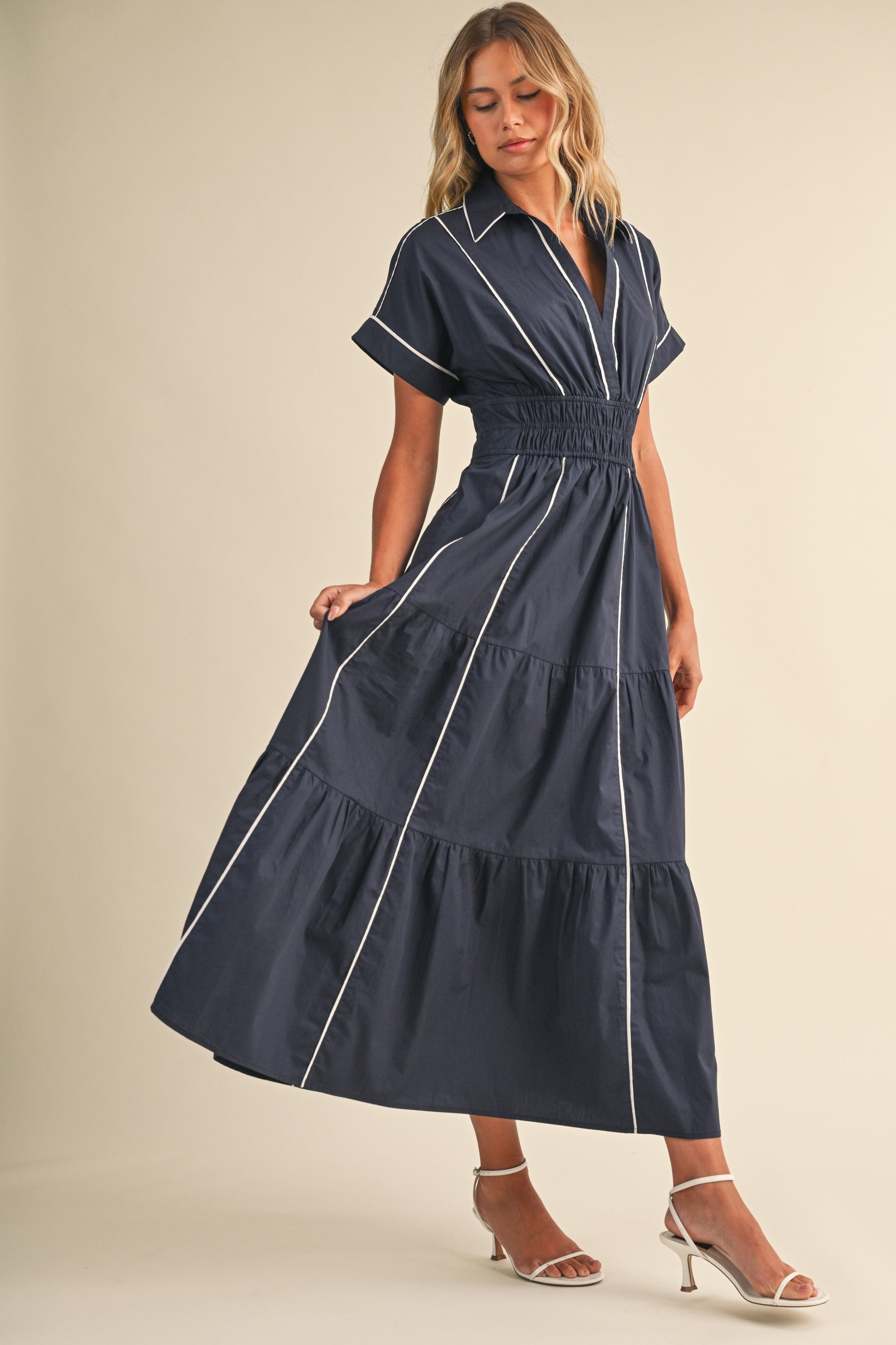 A short-sleeve navy blue shirt maxi dress featuring a classic collar, white vertical contrast piping, a thick smocked elastic waistband, and a tiered A-line skirt.