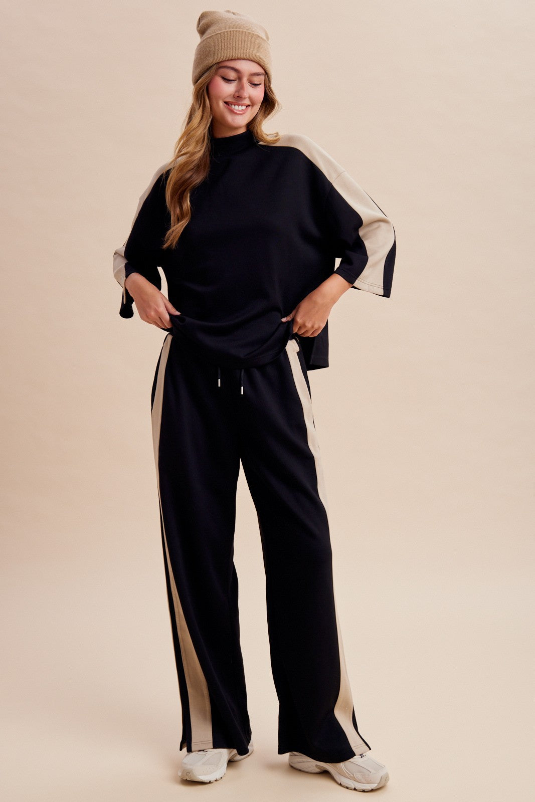 Women's two-piece black lounge set featuring a half-sleeve mock-neck top, neutral side-stripe detailing, and matching wide-leg pants with ankle hem slits.
