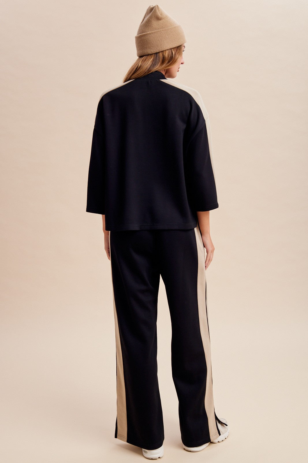 Women's two-piece black lounge set featuring a half-sleeve mock-neck top, neutral side-stripe detailing, and matching wide-leg pants with ankle hem slits.