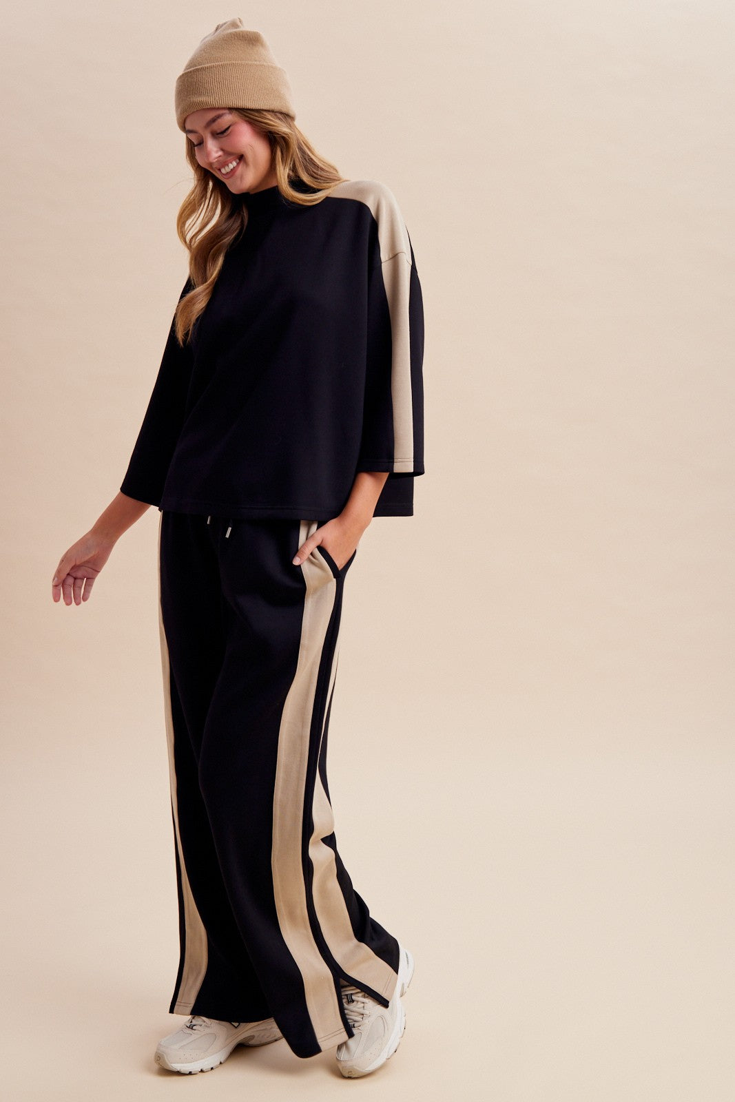 Women's two-piece black lounge set featuring a half-sleeve mock-neck top, neutral side-stripe detailing, and matching wide-leg pants with ankle hem slits.