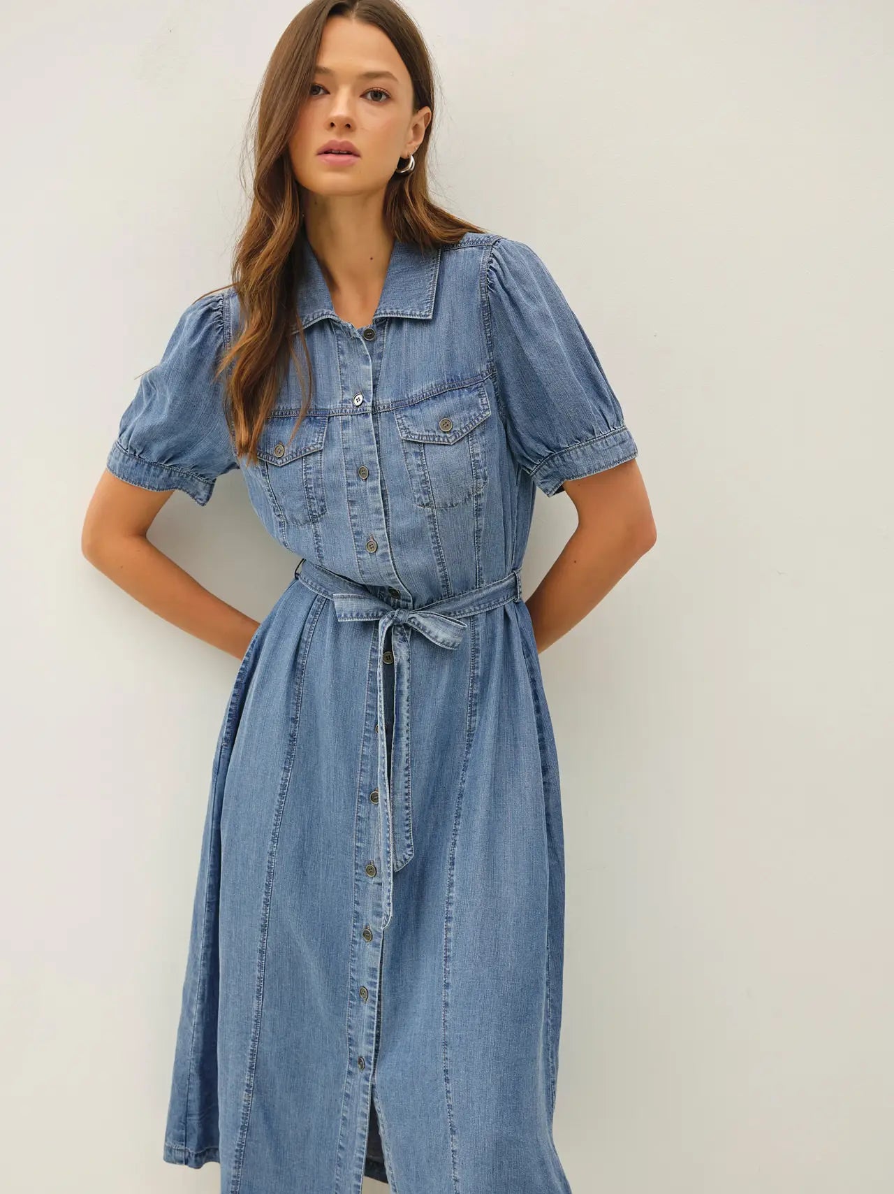 A women's short puff-sleeve denim shirt dress in a light wash featuring a pointed collar, a full button-down front, a matching waist tie belt, and convenient side pockets.