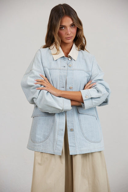 A women's relaxed oversized light wash denim utility jacket featuring a cream-colored pointed contrast collar, a button-front closure, and large front patch pockets with flaps.