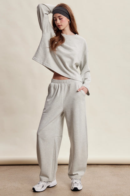 A women's heather gray two-piece stretch cotton lounge set featuring a long-sleeve crewneck top and matching high-waisted relaxed wide-leg pants.