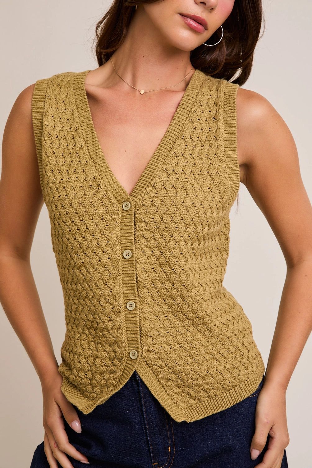 A women's sleeveless olive green button-front vest knit top featuring an intricate textured basketweave pattern, a modest V-neckline, and ribbed trim along the split hem.