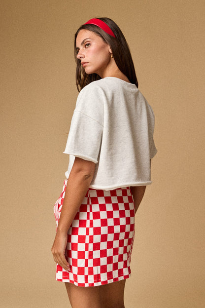 A women's light gray short-sleeve graphic t-shirt featuring a relaxed fit, a raw cut cropped hemline, and a textured patchwork American flag design made from blue star print, red gingham, and white eyelet lace fabrics.