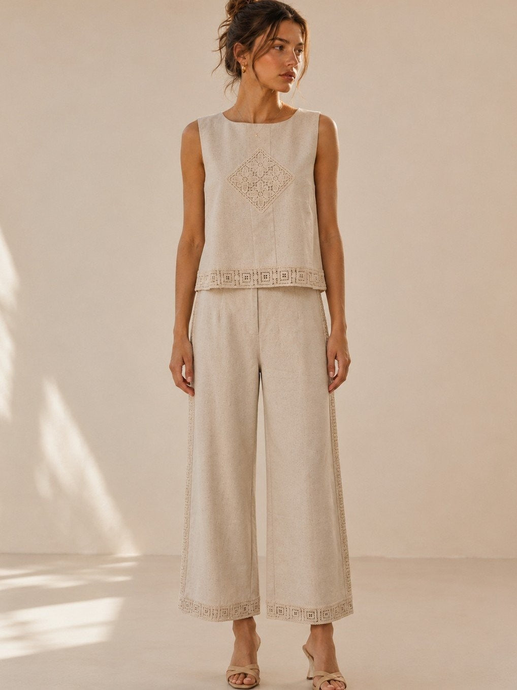 A women's two-piece linen-blend clothing set in an oat color featuring a sleeveless top with a chest diamond crochet applique and matching high-waisted wide-leg pants with lace trim panels along the sides and hems.