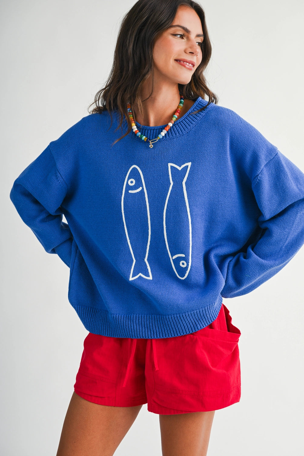 A women's royal blue long-sleeve knit crewneck sweater featuring a white embroidered sardine graphic on the front and ribbed trim along the collar, cuffs, and hem.