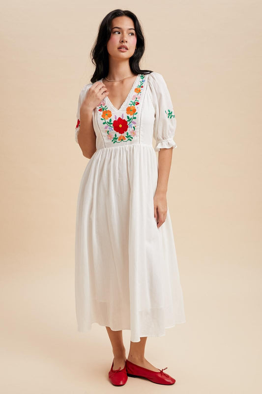Off white maxi dress with a v-neck and embroidered bodice.  The sleeves are cuffed with a ruffle detail and hit just above the elbow with minimal embroidered detail. 