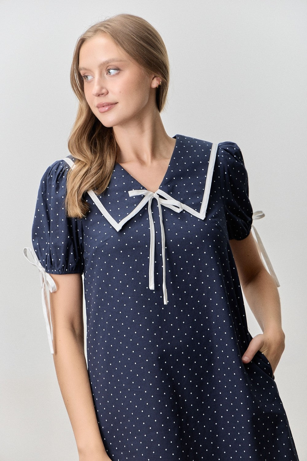 Just above the knee navy dress with white polka dots. 
V-neck with a peter pan collar and a ribbon tie. 
Minimally puffed sleeves with ribbon ties
Ruffled hem 