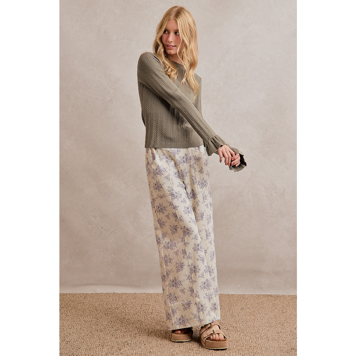 A women's olive green long-sleeve cable-knit sweater featuring a mock neckline, ribbed hem, and ruffled flare knit cuffs.