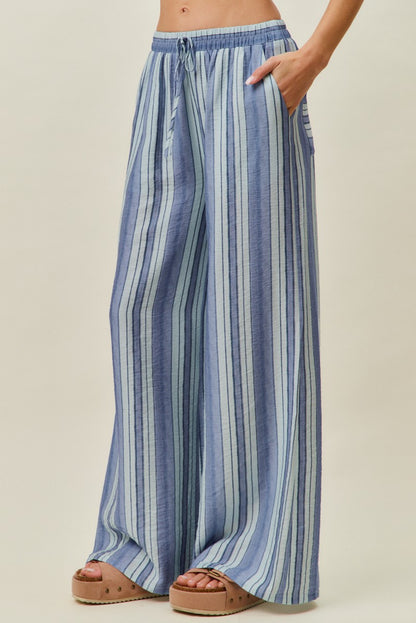 A pair of women's high-waisted wide-leg pull-on pants featuring vertical stripes in shades of blue with a gathered elastic drawstring waistband and side pockets.