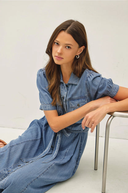A women's short puff-sleeve denim shirt dress in a light wash featuring a pointed collar, a full button-down front, a matching waist tie belt, and convenient side pockets.