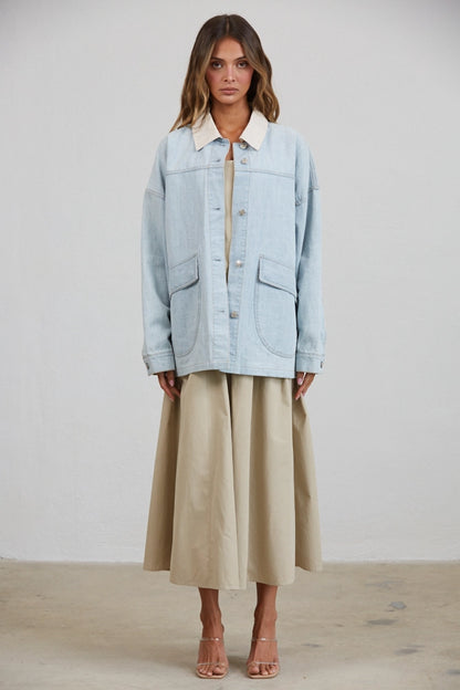 A women's relaxed oversized light wash denim utility jacket featuring a cream-colored pointed contrast collar, a button-front closure, and large front patch pockets with flaps.