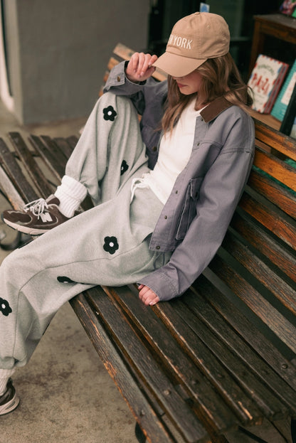 A women's heather gray wide-leg fleece sweatpants featuring an elastic drawstring waistband, relaxed barrel leg, and black chenille flower patches across the front and back.