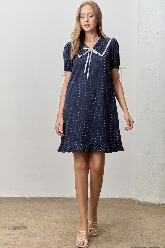 Just above the knee navy dress with white polka dots. 
V-neck with a peter pan collar and a ribbon tie. 
Minimally puffed sleeves with ribbon ties
Ruffled hem 
