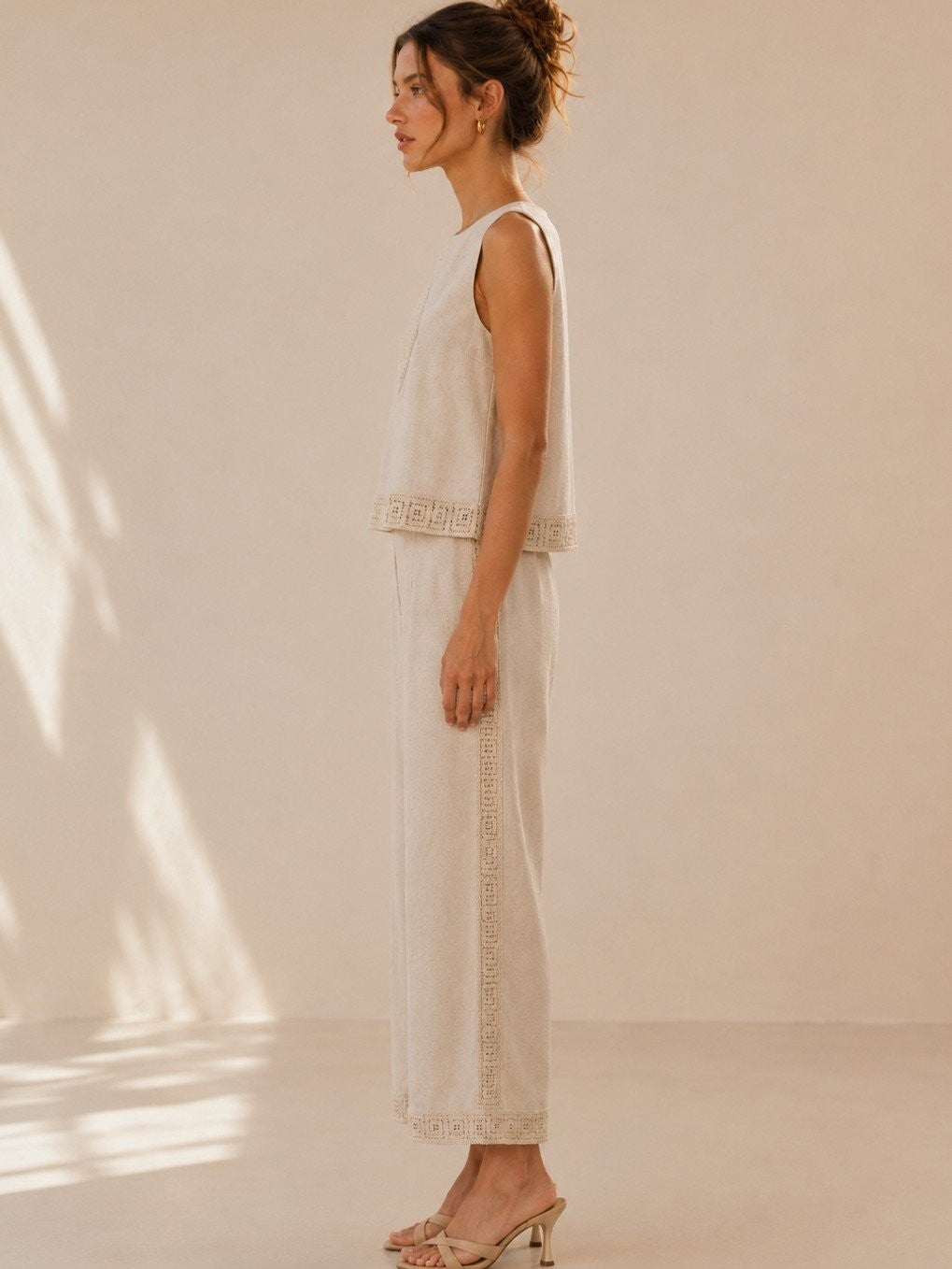 A women's two-piece linen-blend clothing set in an oat color featuring a sleeveless top with a chest diamond crochet applique and matching high-waisted wide-leg pants with lace trim panels along the sides and hems.