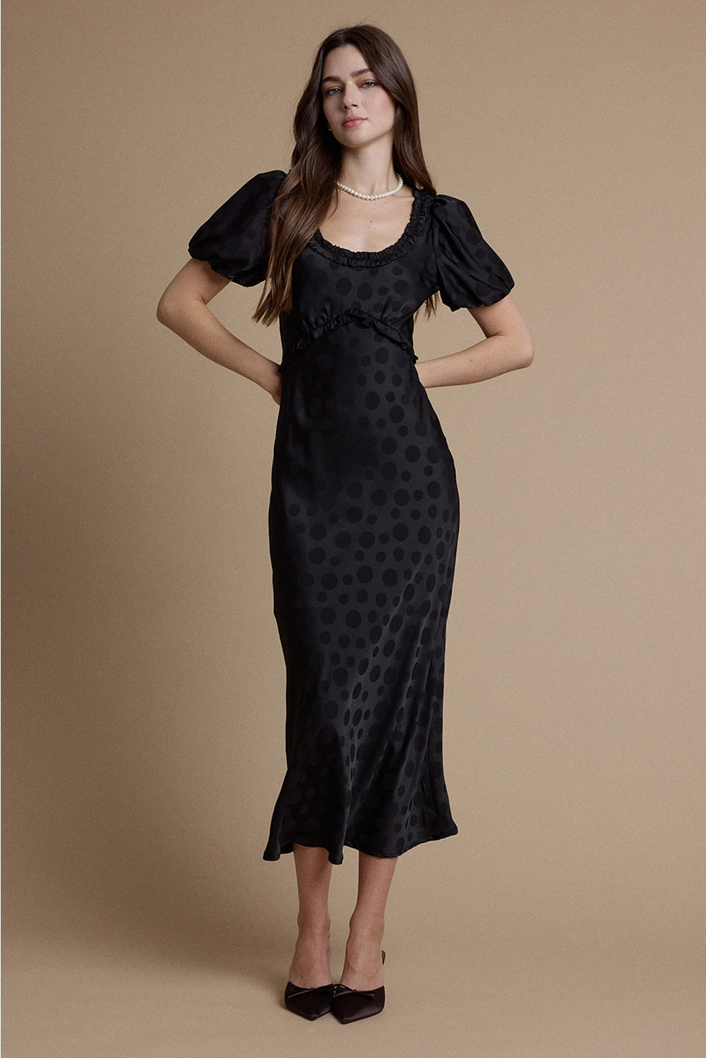 A women's black satin jacquard polka dot midi dress featuring short puff sleeves, a scoop neckline with ruffle trim, and a high empire waistline.