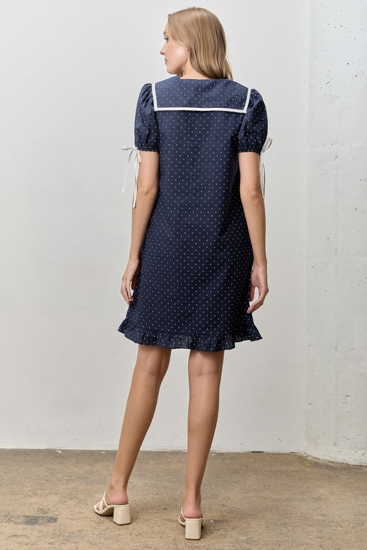 Just above the knee navy dress with white polka dots. 
V-neck with a peter pan collar and a ribbon tie. 
Minimally puffed sleeves with ribbon ties
Ruffled hem 