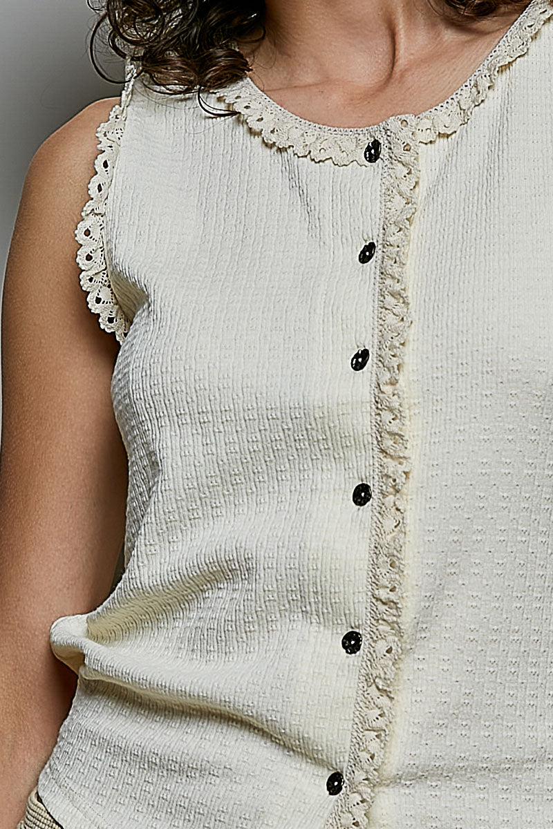 A women's sleeveless cream textured waffle-knit top featuring a button-front closure and delicate eyelet lace trimming along the round neckline and armholes.