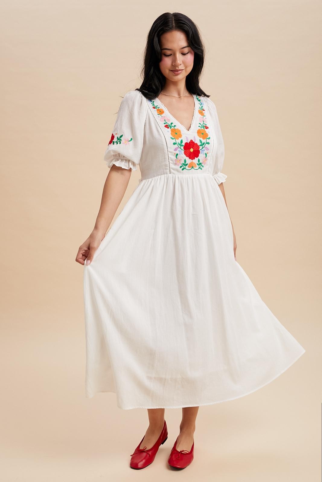 Off white maxi dress with a v-neck and embroidered bodice.  The sleeves are cuffed with a ruffle detail and hit just above the elbow with minimal embroidered detail. Waist tie in the back. 