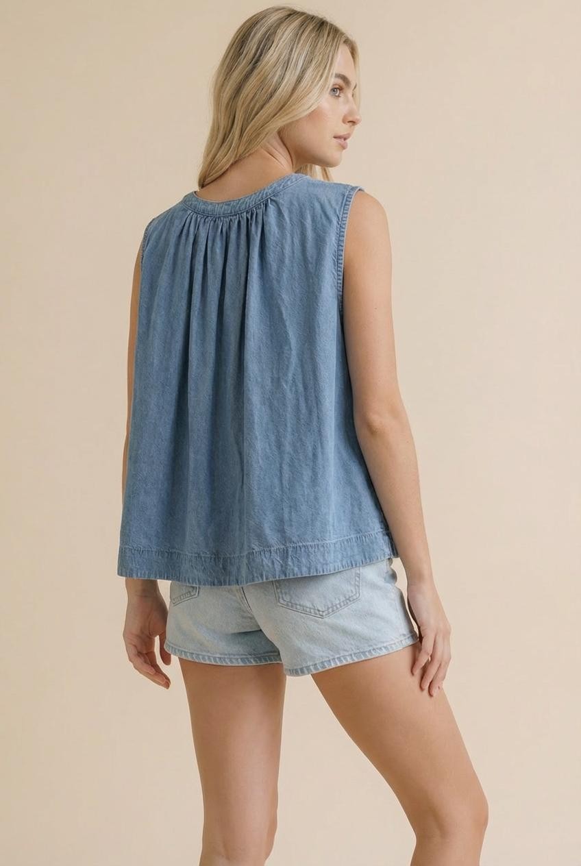 A sleeveless washed blue denim top featuring a functional button-down front, a rounded neckline with shirred detailing, and a relaxed swing silhouette.