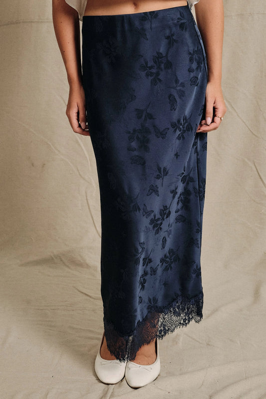 A women's navy blue satin bias-cut slip midi skirt featuring an elastic waistband and delicate scalloped lace trim along the hemline.