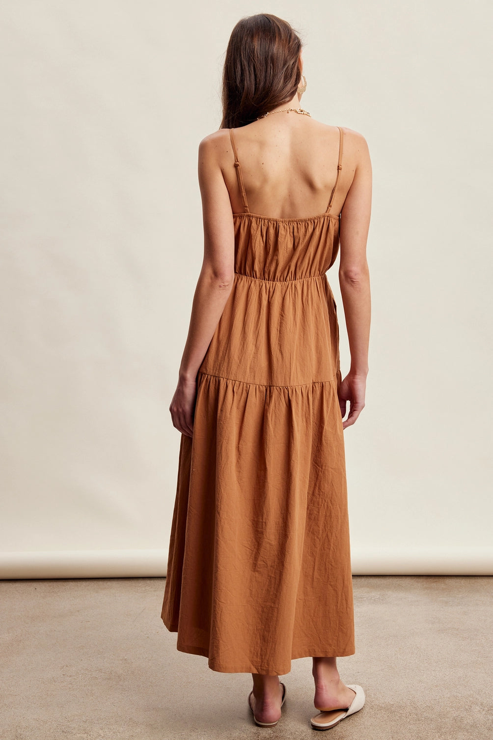 A women's brown sleeveless tiered maxi dress featuring a tonal embroidered floral lace vest overlay with adjustable side tie details.