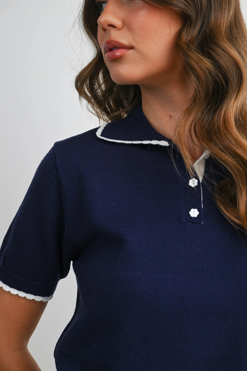 A women's navy blue short-sleeve fine-knit polo top featuring white scalloped contrast trim on the collar, button placket, and sleeve cuffs.