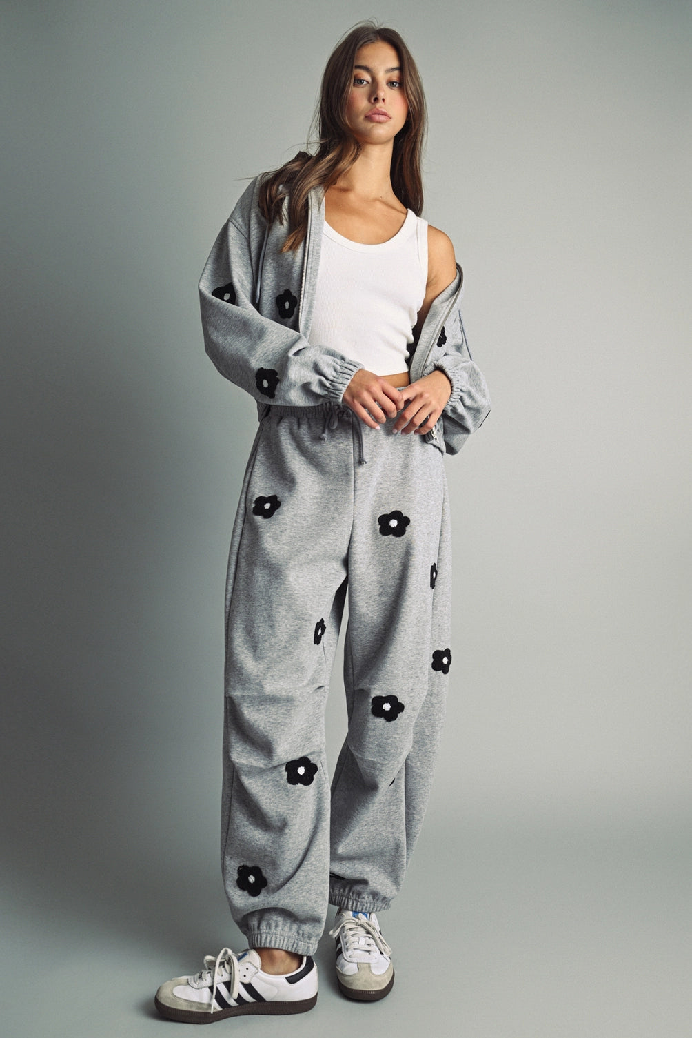 A women's heather gray wide-leg fleece sweatpants featuring an elastic drawstring waistband, relaxed barrel leg, and black chenille flower patches across the front and back.