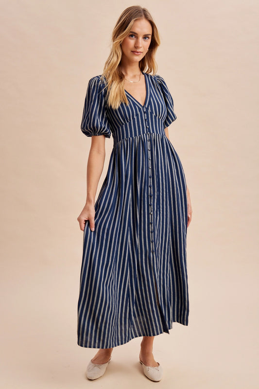 A women's navy blue and cream vertically striped short puff sleeve maxi dress featuring a V-neckline, full front button placket, and high gathered waistline.