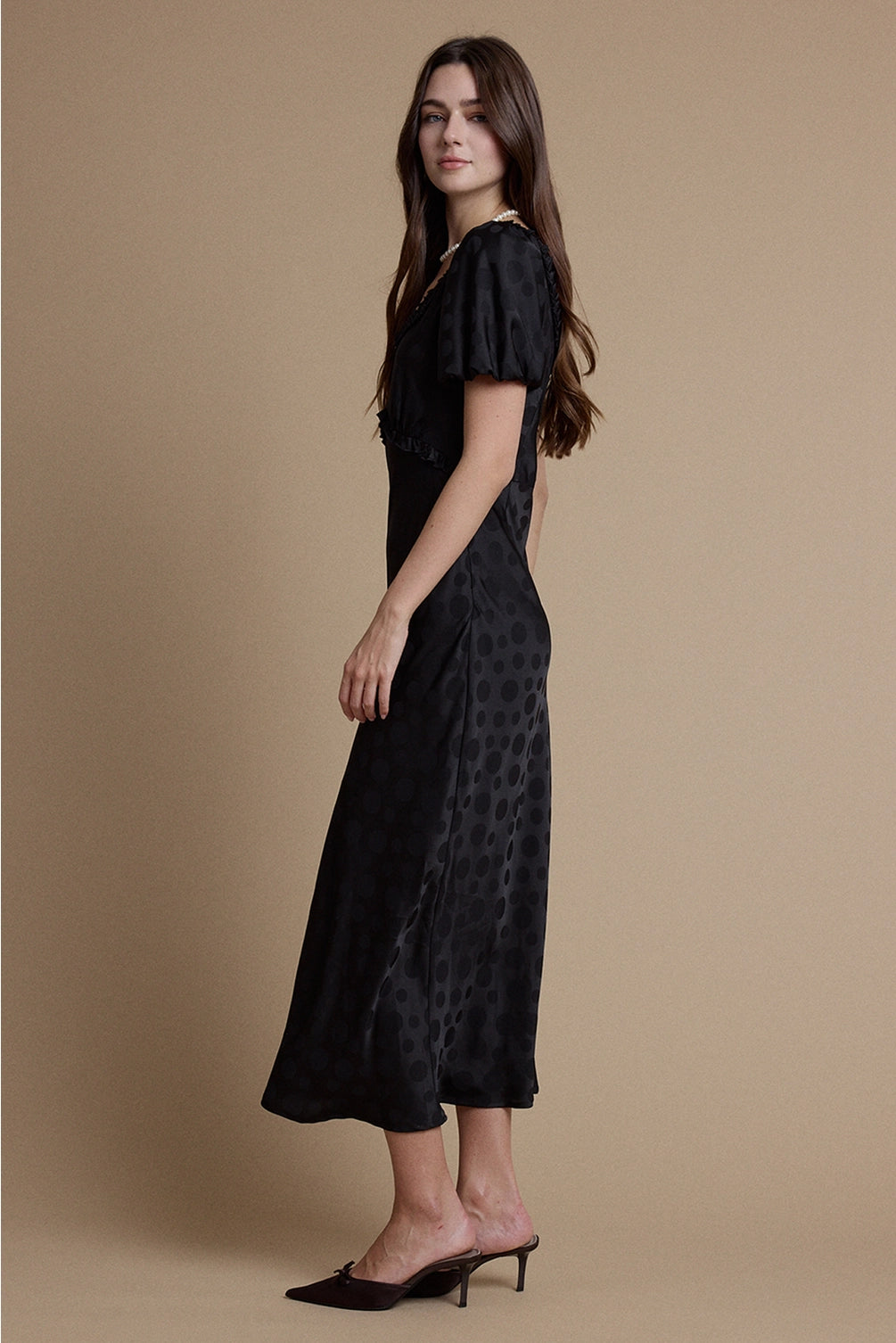 A women's black satin jacquard polka dot midi dress featuring short puff sleeves, a scoop neckline with ruffle trim, and a high empire waistline.