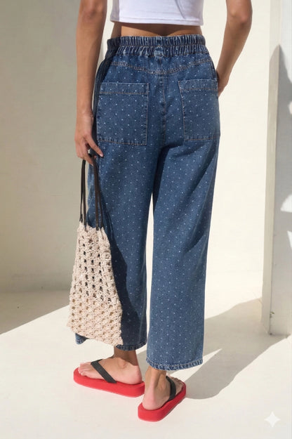 High-waisted wide-leg denim pants featuring an all-over white micro polka dot print, a comfortable smocked elastic waistband, and functional side pockets.