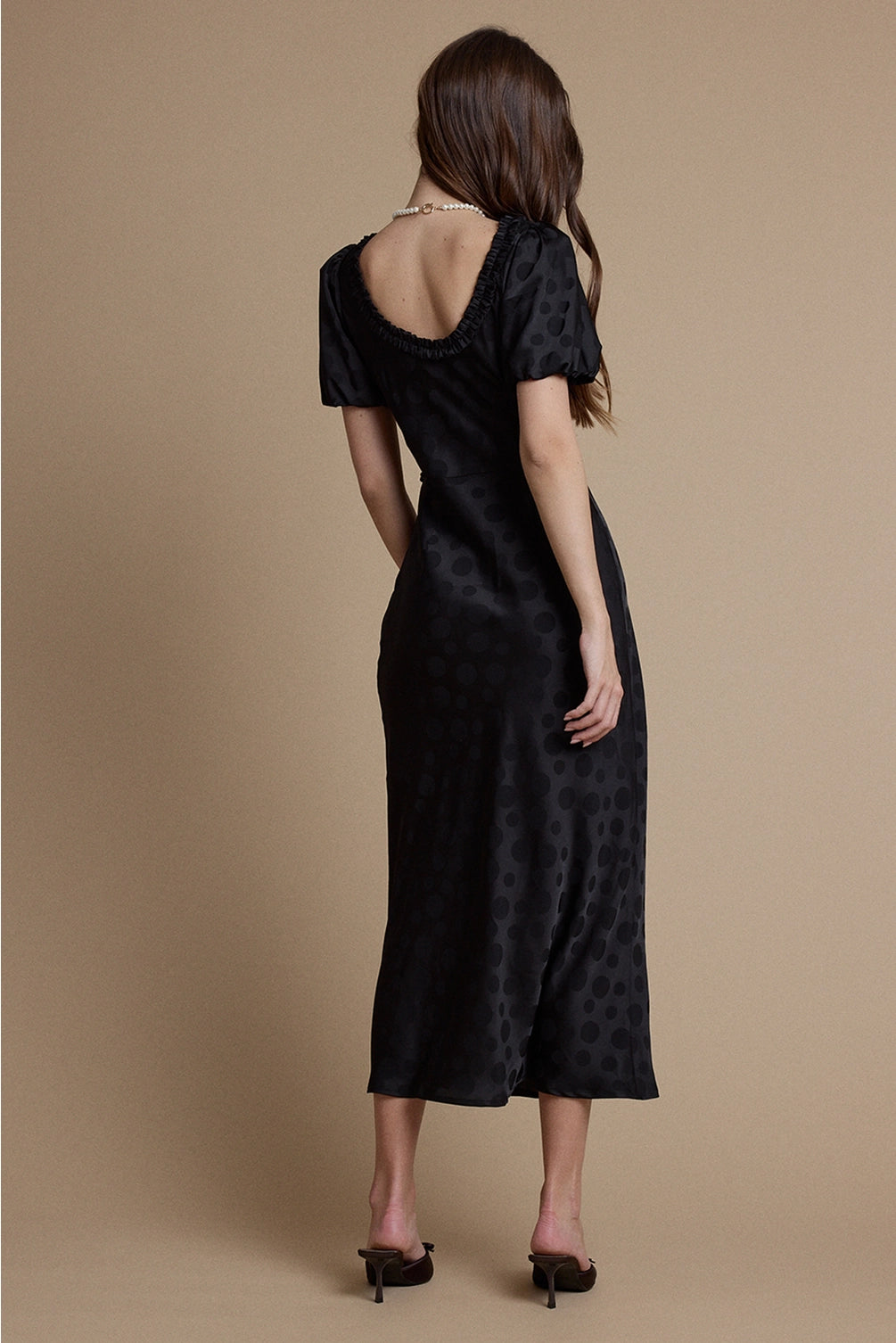 A women's black satin jacquard polka dot midi dress featuring short puff sleeves, a scoop neckline with ruffle trim, and a high empire waistline.